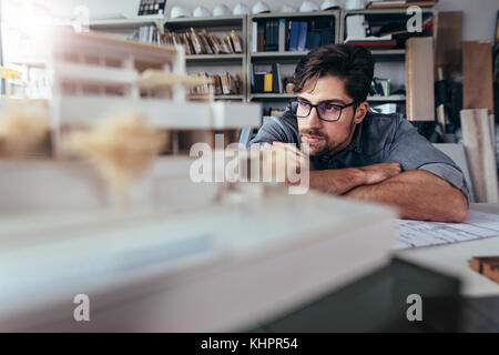Thoughtful male architect in office looking at house model. Young man working on new construction project. Stock Photo