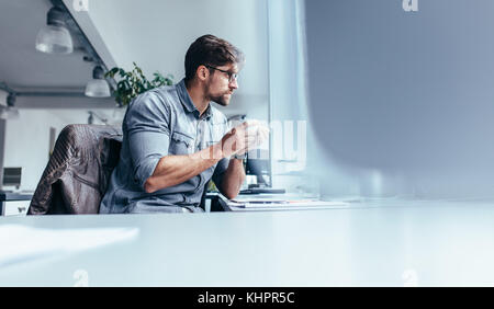 businessman sitting in office with cup of coffee. Young man holding mug and looking away. Stock Photo