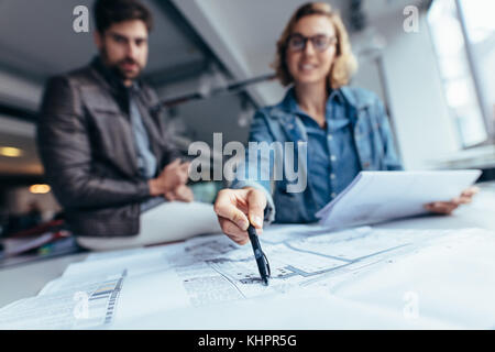 Designers working on blueprint on table in office. Focus on female hand pointing on drawing. Stock Photo