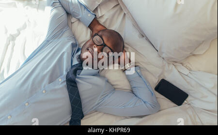 Man in formal clothes relaxing on bed with his eyes closed. Top view of a businessman relaxing. Stock Photo