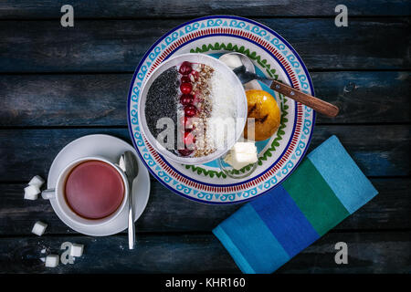 Sweet rice porridge with berries nuts and coconut chips, top view. Healthy breakfast or dessert. Tea and bread with butter on a colored wooden backgro Stock Photo