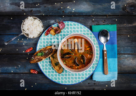 Seafood tomato soup with bread and rice for a garnish on a colored wooden background. Top view. Stock Photo