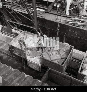 1950s, historical picture from overhead showing male workers in an LMS wagon putting sheets of heavy metal cargo bound for Copenhagen onto chains for loading onto a ship, England, UK. Stock Photo