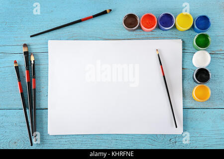 Various paints, brushes, white sheets paper on wooden blue background. Top view. Free space for text. Stock Photo