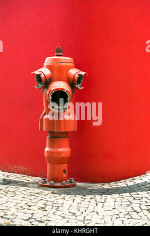 Red fire hydrant against a red wall in Funchal, Madeira, Portugal Stock Photo
