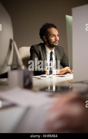 Portrait shot of mixed race bearded manager wearing stylish suit preparing presentation with help of computer while sitting at desk, interior of moder Stock Photo