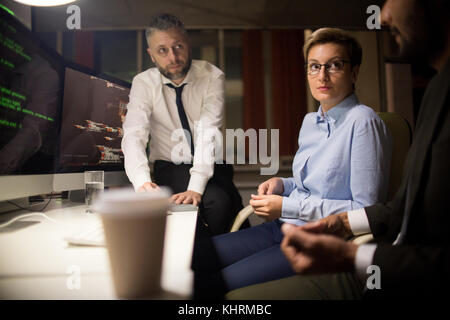 Profile view of bearded software developer sharing ideas concerning joint project with colleagues while having working meeting at dim open plan office Stock Photo
