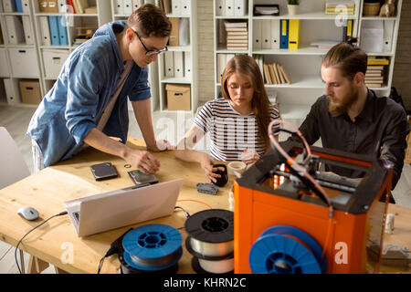 Group of hard-working students working on joint project: they gathered together at modern laboratory and printing 3D models Stock Photo
