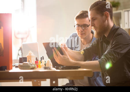 Profile view of bearded young engineer showing work results to his colleague with help of digital tablet while having working meeting at modern labora Stock Photo