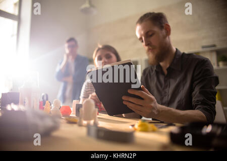Team of creative designers having productive project discussion in modern laboratory, small 3D printed prototypes located on desk Stock Photo
