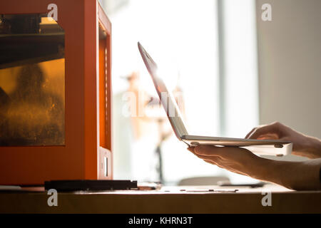 Close-up shot of unrecognizable designer sitting at office desk and working with 3D printer, lens flare Stock Photo
