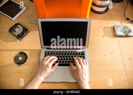 Unrecognizable engineer sitting at office desk and adjusting setting of 3D printer with help of laptop, close-up shot Stock Photo