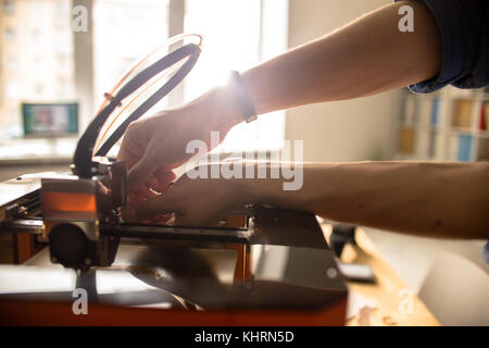 Close-up shot of unrecognizable man wrapped up in repairing 3D printer after breakage, interior of modern office on background Stock Photo
