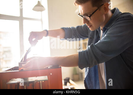 Profile view of concentrated young engineer making necessary preparations for productive work with 3D printer, interior of modern laboratory on backgr Stock Photo