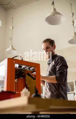 Low angle view of handsome bearded designer using 3D printer while working on ambitious project, interior of modern studio on background Stock Photo