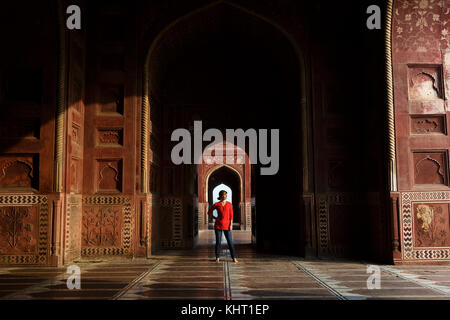 Caucasian woman in red shirt standind at the arch, Taj Mahal, UNESCO World Heritage Site, Agra, Uttar Pradesh, India, Asia. Stock Photo