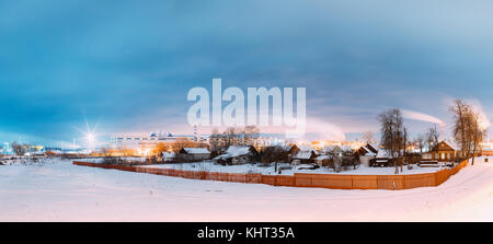 Dobrush, Belarus. Panorama With Old Houses On Background Of A Paper Factory Or A Industrial Plant On A Winter Evening Or Night. Stock Photo