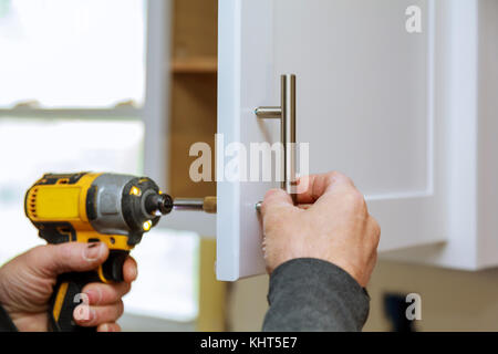 The worker sets a new handle on the white cabinet with a screwdriver Stock Photo