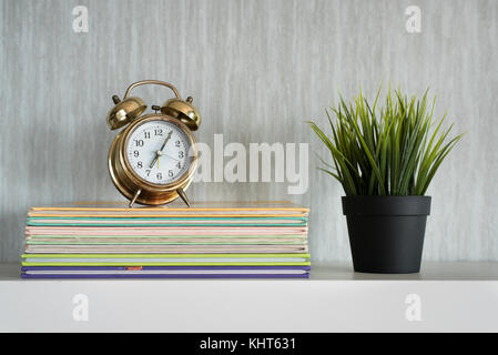encyclopedia books, plant and alarm clock on white shelf - organized concept Stock Photo
