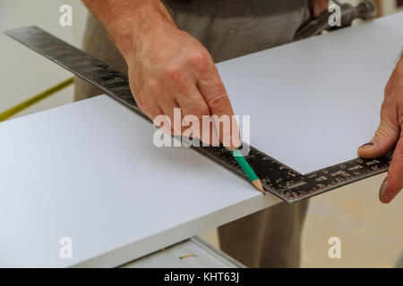 Hand of a carpenter measures the distance using a builder's square and marks Stock Photo