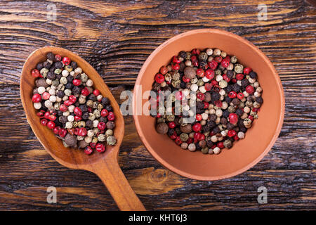 Multicolored peppers peas in a spoon and a plate on a brown wooden table Stock Photo
