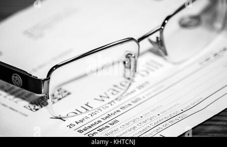 A pair of DNKY reading glasses placed on top of a water bill. Black & white image. Stock Photo