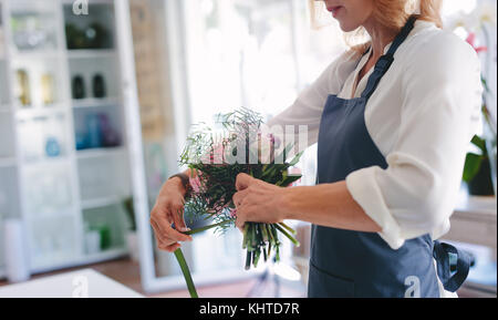 Skillful female florist creating bouquet of flowers. Young woman florist arranging flowers at workshop. Stock Photo
