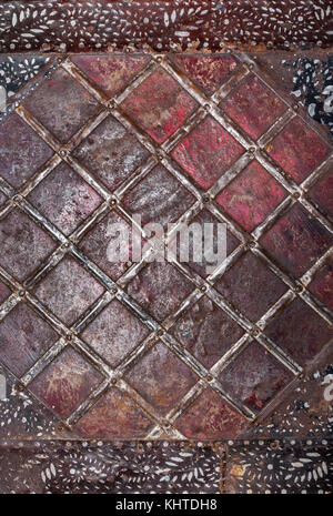 Painted in red shabby, scratched and rusty metal sheet and nailed to it tin strips in form of rhombus. Stock Photo