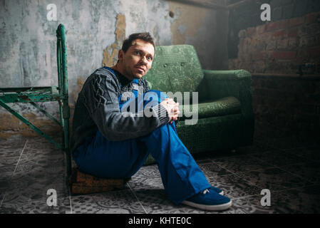 Depressed man in uniform sitting on the floor in dark room, psycho patient. Mentally ill people concept, stressed human Stock Photo