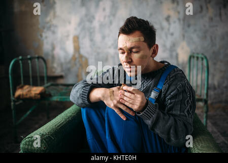 Madman in uniform with plasters on face and hands, psycho patient. Mentally ill people concept, crazy human Stock Photo