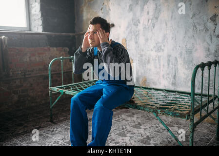 Disturbed madman sitting on a rusty bed, face sealed with plaster, depressed psycho patient. Mentally illness concept, crazy human Stock Photo