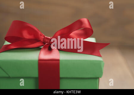 green paper gift box with red ribbon bow on oak table Stock Photo