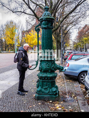 Berlin Schöneberg.Senior elderly man using historic old water fountain On Winterfeldtplatz Stock Photo