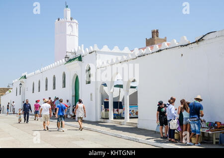 Asilah, Morocco - August 14 2013: Unidentified tourists walking and shopping in front of white mosque and city walls Stock Photo