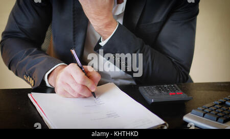 Unrecognizable businessman sitting at his desk in the office and writing on sheet of paper Stock Photo