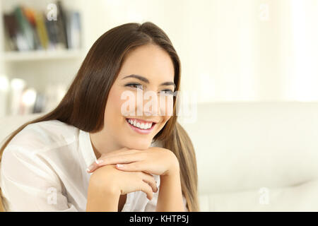 Portrait of a happy home owner woman with perfect teeth smiling sitting on a sofa in the living room in a house interior Stock Photo