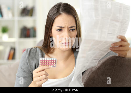 Worried woman reading contraceptive pills leaflet sitting on a couch at home
