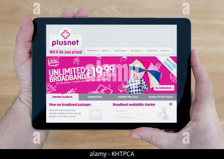 A man looks at the Plusnet website on his iPad tablet device, shot against a wooden table top background (Editorial use only) Stock Photo