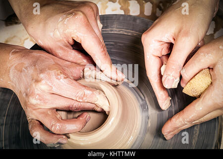 Close-up of a young woman potter is teaching a woman to sculpt on a pottery wheel a vase of brown clay in a creative workshop, top view Stock Photo