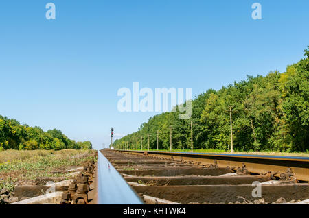 old railway closeup and trees along it under deep blue sky Stock Photo
