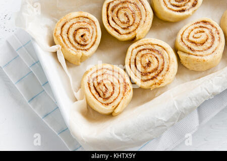 Cinnamon rolls or cinnabon, homemade recipe raw dough preparation sweet traditional dessert buns pastry food. Raw cinnamon rolls ready for baking. Stock Photo