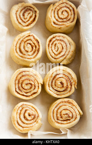 Cinnamon rolls or cinnabon, homemade recipe raw dough preparation sweet traditional dessert buns pastry food. Raw cinnamon rolls ready for baking. Stock Photo