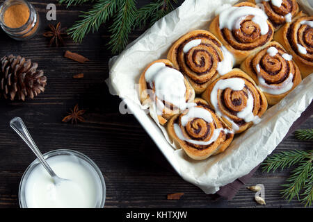 Cinnamon rolls or cinnabon for Christmas. Homemade traditional winter festive dessert buns pastry on dark wooden background. Stock Photo