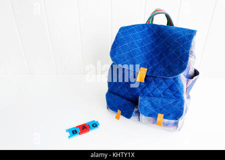 Blue bag with puzzle letters on white table. Hand made backpack. Stock Photo