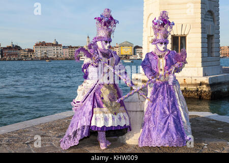 Venice Carnival 2017, Veneto, Italy, Two women in purple posing in front of the lighthouse on San Giorgio Maggiore with copy space Stock Photo