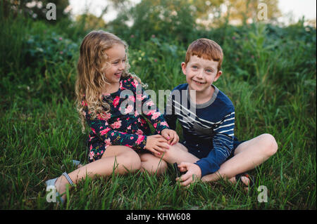 Girl and brother sitting in field Stock Photo