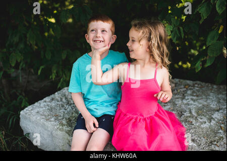 Girl with hand on brother's chin, sitting on rock Stock Photo