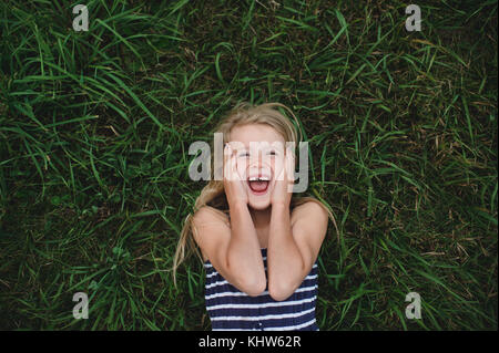 Overhead portrait of girl lying on grass with hands on her cheeks