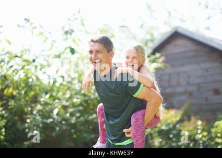 Father giving daughter piggyback in garden Stock Photo