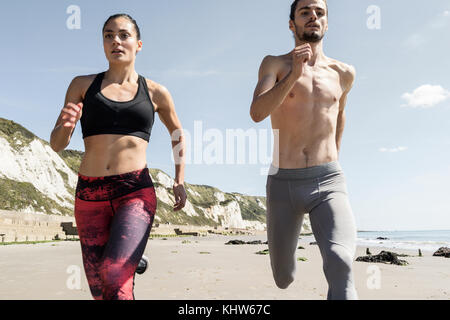 Young man and woman running along beach, front  view